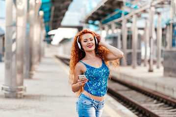 Attractive white young woman about 25 years old in shorts and hoodie is walking during the street in Saint-Petersburg with paper cup of coffee in hands and looks happy and cheerful.