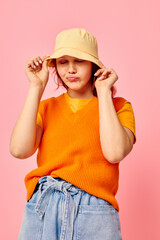 funny girl in an orange sweater in yellow hat talking on the phone pink background unaltered