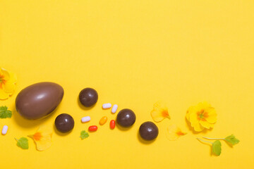 Easter yellow background with chocolatte eggs,    candy and spring flowers