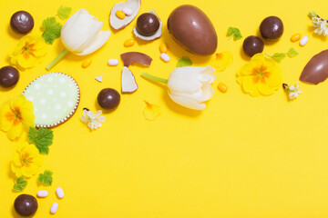 Easter yellow background with chocolatte eggs,    candy and spring flowers