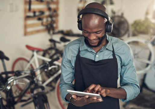 We need good music in this store. Shot of a handsome young man standing alone in his bicycle shop and using a digital tablet while wearing headphones.