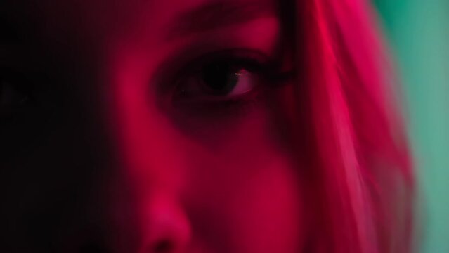 Extreme close-up beautiful female eyes looking at camera in neon red lights. Posing for a fashion magazine. Close-up girl's sly look