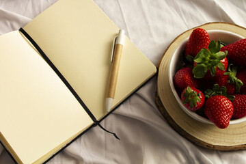 Blank notebook, pen and strawberries on white sheet. Flat lay, top view