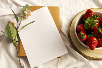 Blank notebook, flowers and strawberries on white sheet. Flat lay, top view