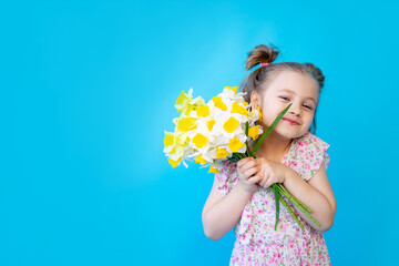a little child girl on a blue isolated studio background with yellow spring flowers daffodils. Space for copying text. Cute kid