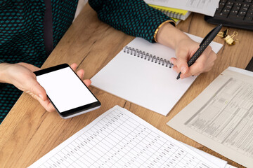 Fototapeta premium Woman writing down business information while using smartphone