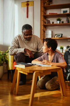 An African-American grandfather is sitting at home with his grandson and helping him with homework.