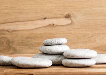 Fototapeta na wymiar Minimalist beauty products background concept. Gray color flat sea stones stacked like an pedestal lot of copy space on oak wood background.