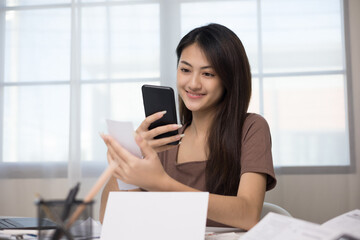 A young Asian woman with many expense bills and she using smartphone to calculate and purchase with scan qr code payment online.