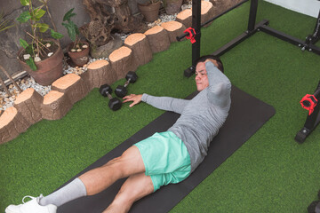 A fit asian guy does oblique crunches while lying on a black mat. Leg raised for added challenge....