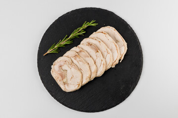 Pieces of pork roll with rosemary sprig on a black plate with a white background.