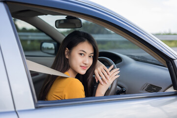 Fototapeta na wymiar Young beautiful asian women getting new car. she very happy and excited. she sit and touching every detail of car. Smiling female driving vehicle on the road