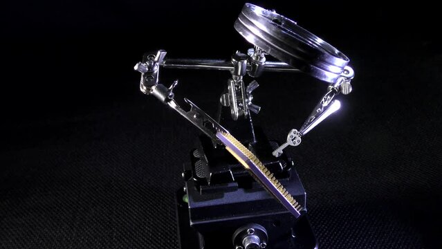 Cpu processor chip in clip holder with magnifying glass.
Adjustable third hand stand with solid heavy base on black background.