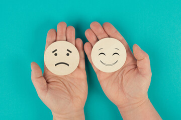 Holding two wooden circles in the hands one face is sad the other one is smiling, positive and negative emotions, rating concept, choosing the mood