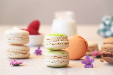 Close up of traditional French macarons with colorful flowers of spring and spoon of sugar cube with raspberries and bottle of milk in background 