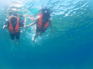 An underwater scene of two persons holding hands while snorkeling in deep blue ocean marine, the water in turquoise color   