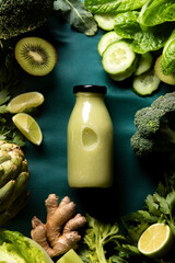 Green detox smoothies in a bottle lying down on a dark table with ingredients