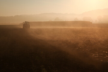 Farmer is ploughing his field on a tractor on a foggy morning where there is steam coming of his fields and is illuminated by the bright sunshine.
