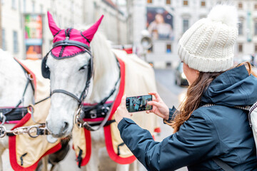 Tourist girl taking photos in Vienna, Austria. Horse-driven carriage at street.