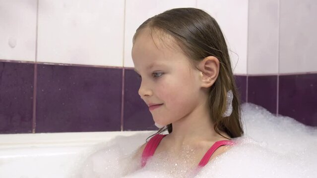 Beautiful girl in a pink swimsuit with a lot of foam in the bath.She plays with foam on her hands.