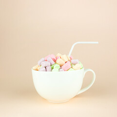 Beautiful variety of marshmallows looks like macaroons in porcelain white coffee cup mug with straw on pastel pink background. Brignt macarons for sweet break.
