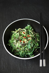 green wakame salad on a plate, with chopsticks black background