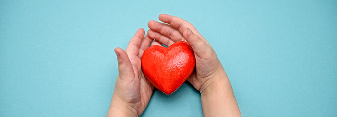 A red heart in the hands of a child on a blue background. The concept of love, care, health and charity.