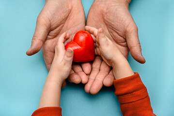 Adult and children's hands holding a red heart - the concept of health, love and family. Mother's...