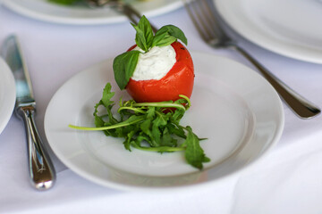 Mozzarella in tomatoes. Caprese salad with mozzarella, tomato, basil and balsamic vinegar arranged on white plate.