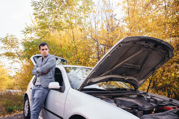 A man looks under the open hood of a car. The car broke down on the road.