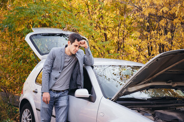 A man looks under the open hood of a car. The car broke down on the road.