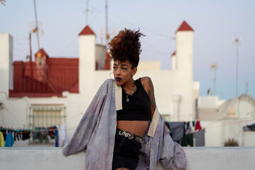 Stylish black female with curly hair and black lips wearing a kimono while resting on terrace...