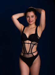 Fototapeta premium Woman posing in seductive black lingerie. Attractive beauty lady advertising underwear slim body on dark blue background free space for text