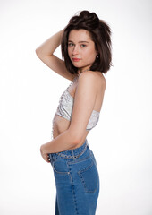 A beautiful woman posing in a jewelry bra with chains and blue jeans isolated on white background. Mockup for party or dance concept with space for text