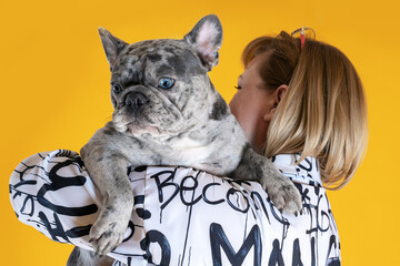 Middle aged woman embracing beautiful young French Bulldog of unusual grey merle spotted color....