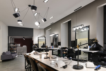 Modern interior of the beauty salon which consist of nail salon and barbershop with black lamps and concrete wall. Mirrors, chairs, backwashes and other equipment are in the salon.