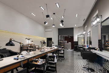 Modern interior of the beauty salon which consist of nail salon and barbershop with black lamps and concrete wall. Mirrors, chairs, backwashes and other equipment are in the salon.