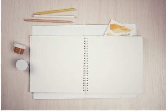 Blank notebook on rings with pencils and paints, artist's desktop, mockup