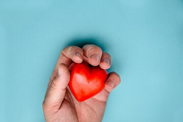 The red heart is squeezed by a man's hand. Top view on a blue background.