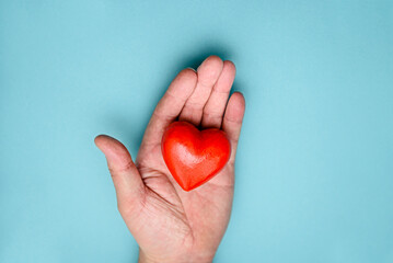 Red heart in hand on a blue background top view. The concept of health, donation and charity.