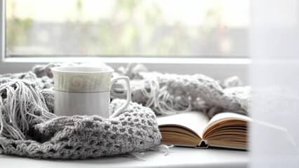 Cozy home with cup of coffee and a book. Hygge style. Mug of black coffee wrapped in warm scarf on wooden board. Top view, vintage style, Still life.