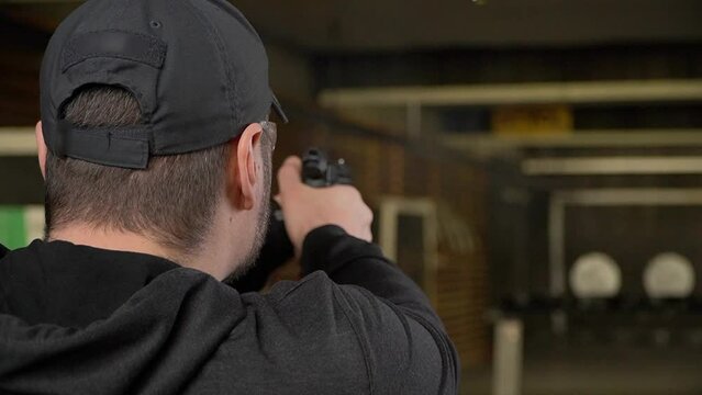 The shooter shoots a pistol in a shooting range, rear view, the pistol and plates are out of focus, the focus is on the shooter's head, soft focus