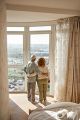 Elderly couple hug and look at city from window