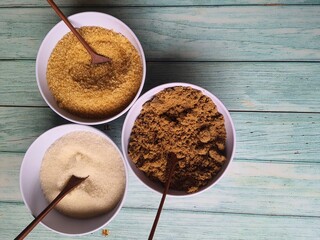 Granulated sugar, demerara and brown sugar in crockery bowls on an old wooden table. View from above.