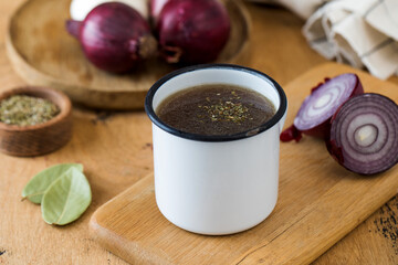Healthy homemade bone broth in a white mug on a wooden board with spices.