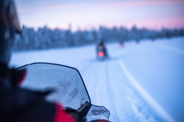 Snowmobiling on the frozen lake at sunset at Torassieppi, Lapland, Finland