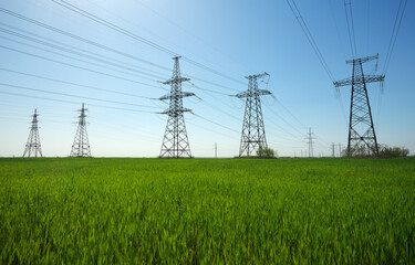 High voltage lines and power pylons in a flat and green agricultural landscape on a sunny day with...