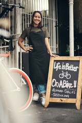Come on in. Full length shot of an attractive young woman standing outside her bicycle shop during...