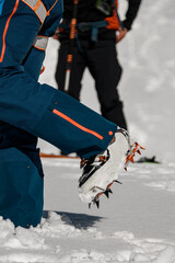 Naklejka premium Close-up of leg of man with climbing crampons over mountaineering shoes for walking through glacier.