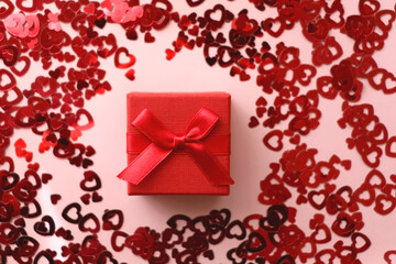 Small red giftbox and heart confetti on pale pink background. Flat lay.